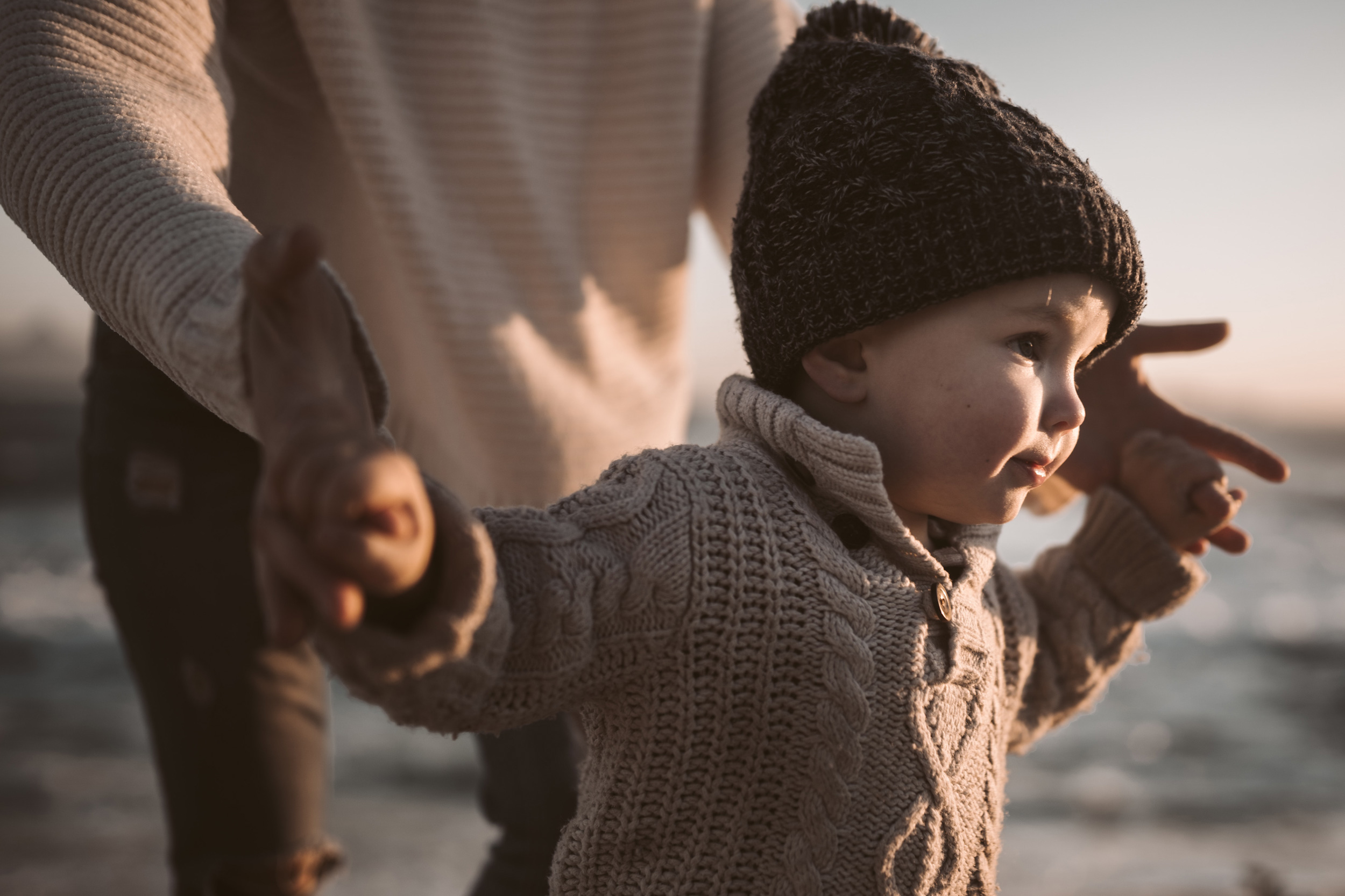 parent holding child's hands as they walk along the beach